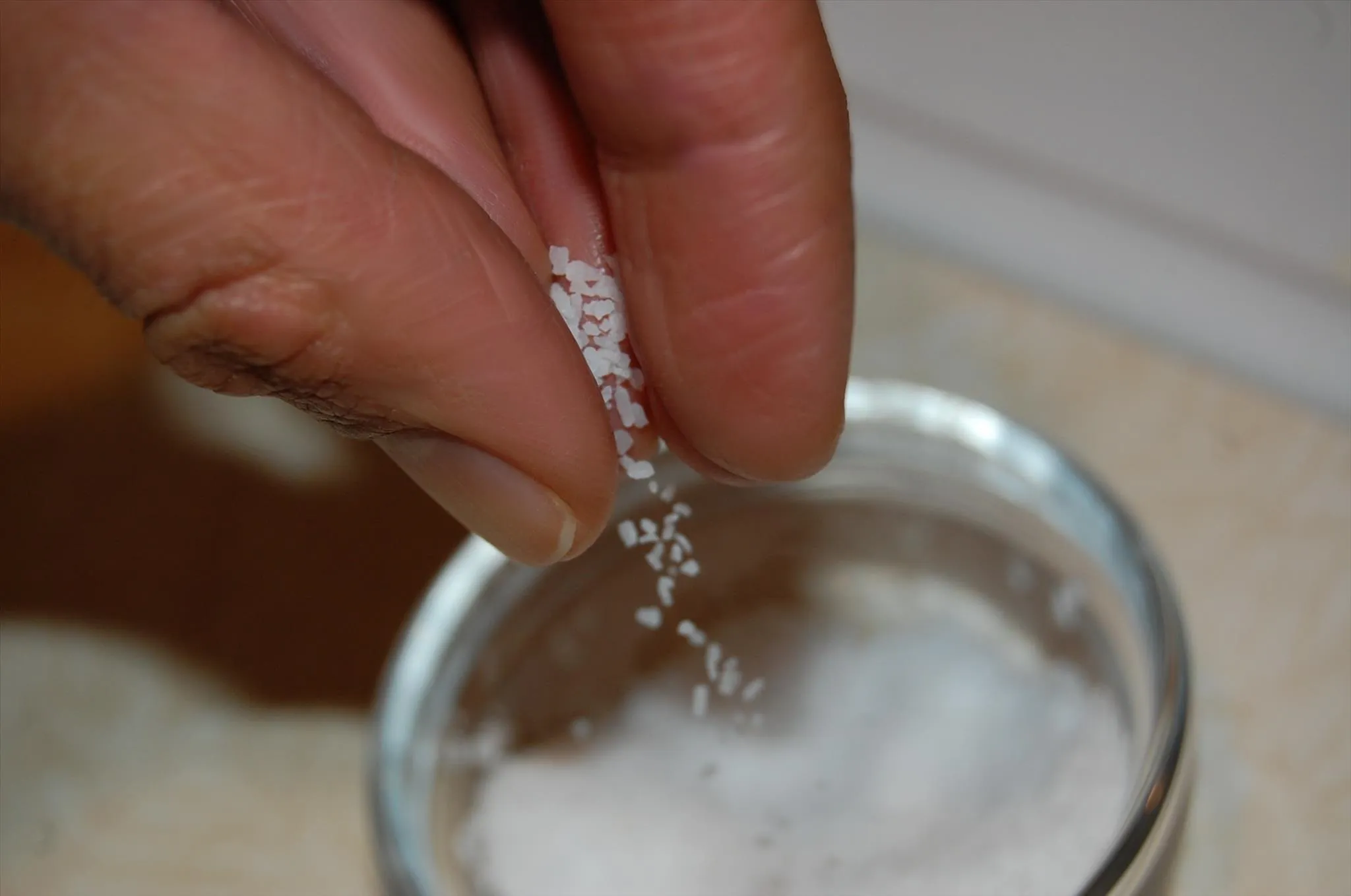 Hand sprinkling salt over a glass container.