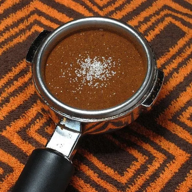 Portafilter filled with ground coffee on a patterned surface.