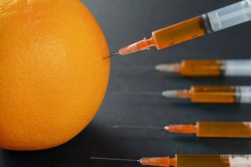 Syringes injecting an orange fruit.