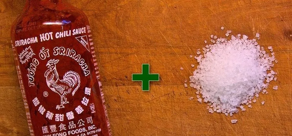 Sriracha hot chili sauce and salt on a wooden surface.