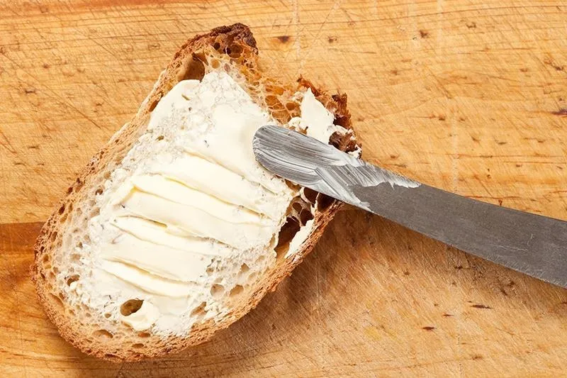 Sliced bread with butter spread on a wooden cutting board.
