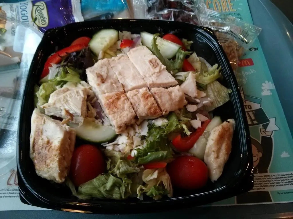 Grilled chicken salad with mixed greens, tomatoes, cucumbers, and bread.