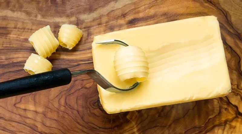 Butter on a wooden cutting board with a butter cutter and curls of butter.
