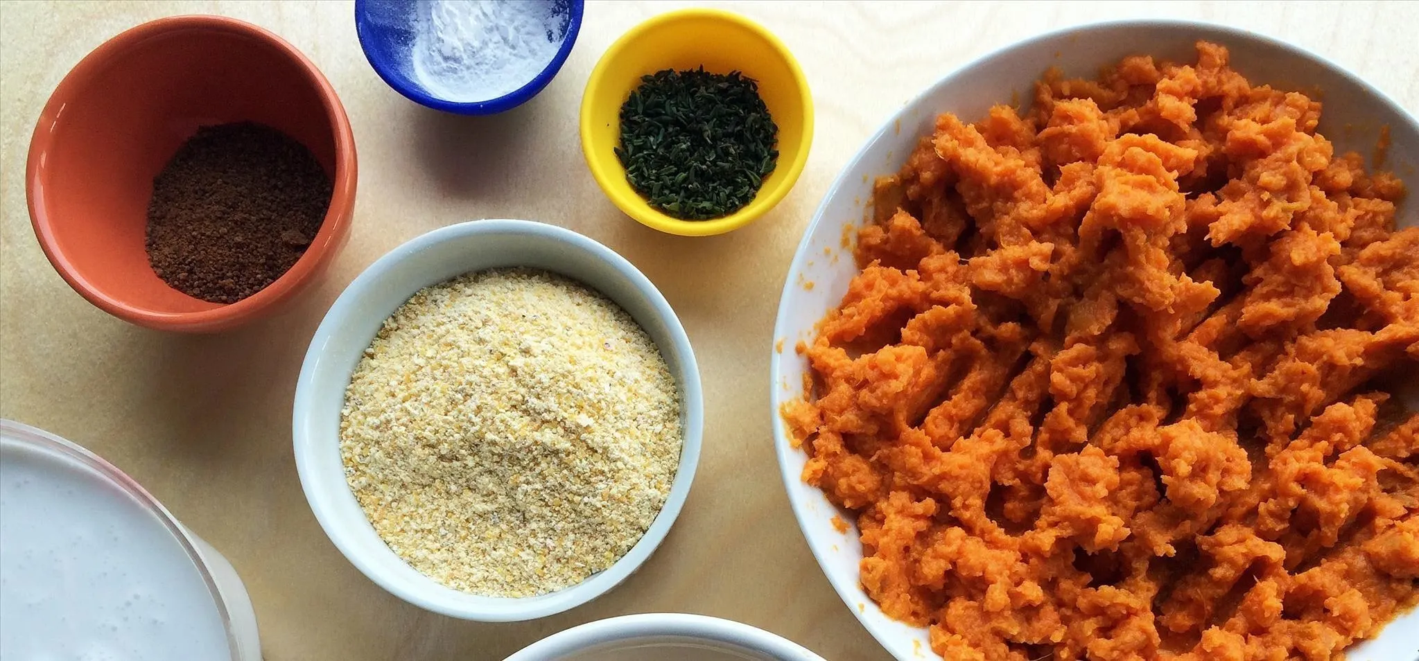 A variety of spices and ingredients including mashed orange sweet potatoes, couscous, and seasonings arranged in bowls.