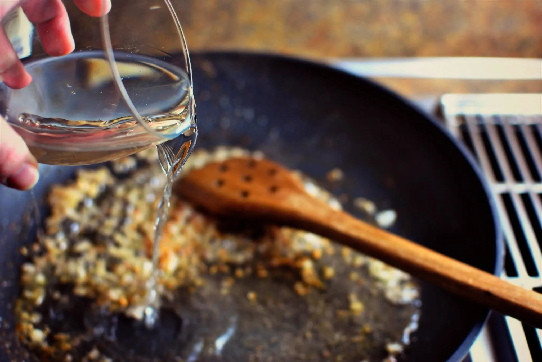 Pouring liquid into a frying pan with sautéed ingredients.
