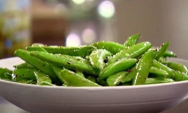Fresh green snap peas garnished with seasoning in a white bowl.