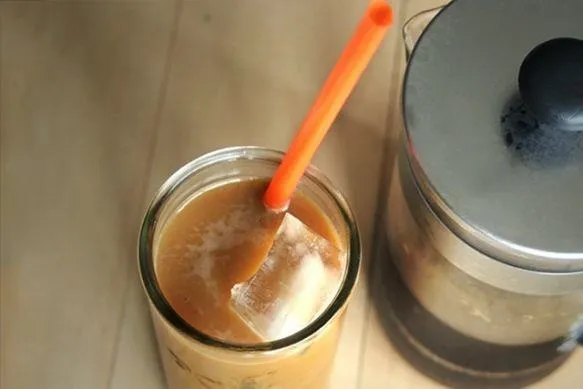 Iced coffee with a stirrer in a glass and a French press in the background.