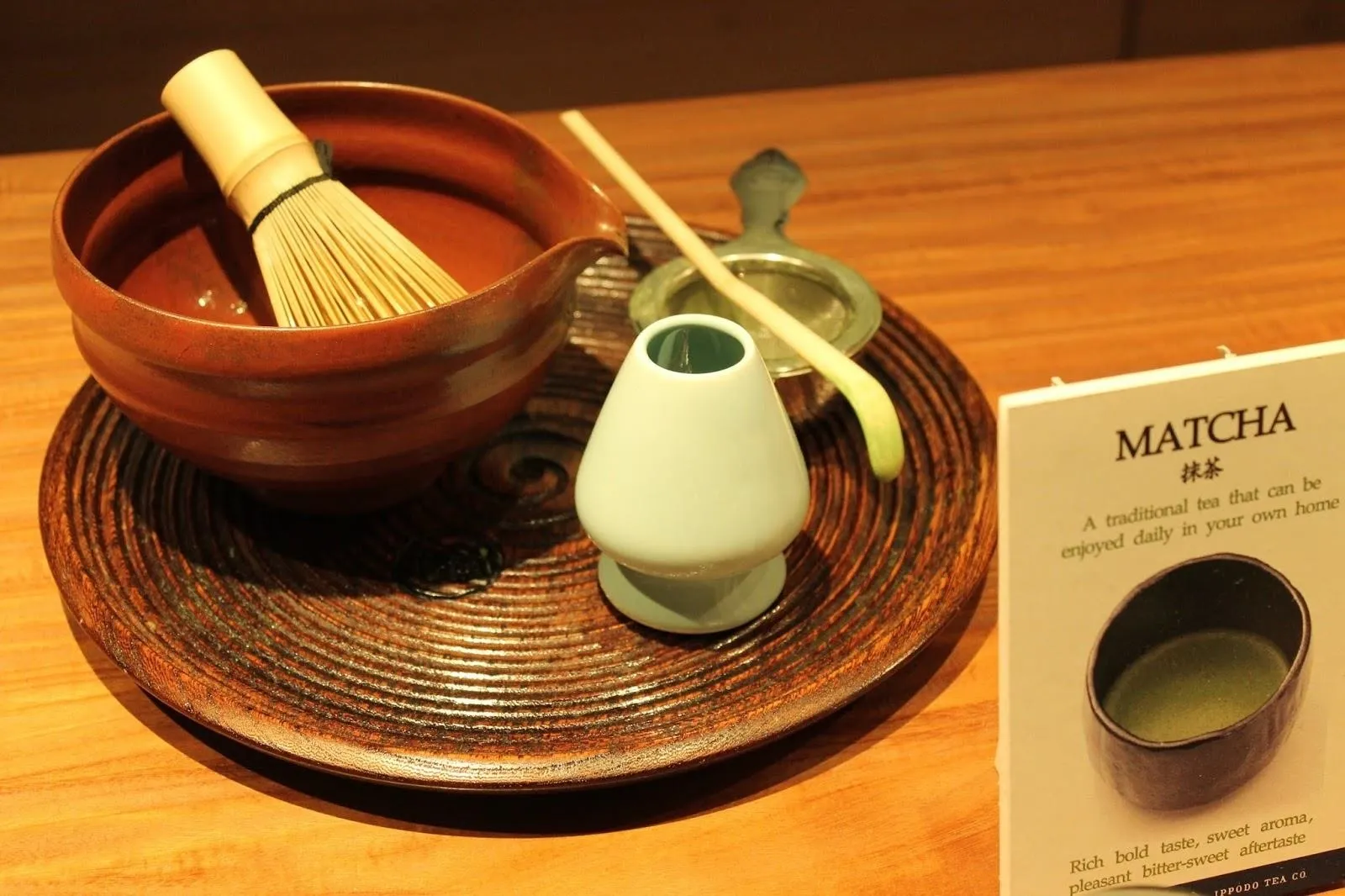 Matcha tea preparation tools, including a bowl, whisk, scoop, and cup on a wooden tray.