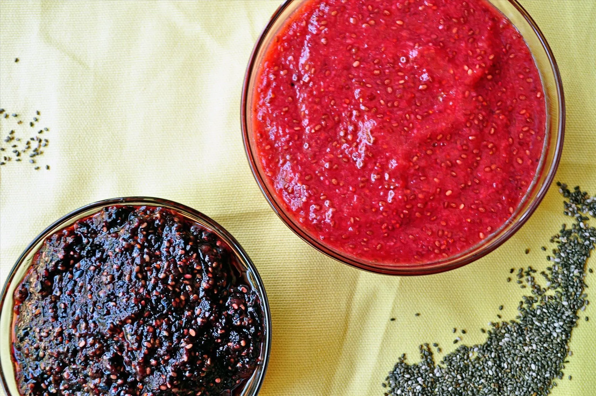 Two bowls of colorful condiments, one red and one dark, placed on a yellow background.