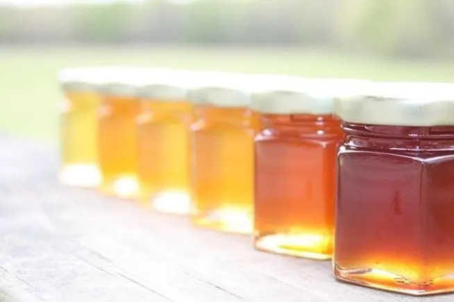 Jars of honey in various shades on a wooden table.