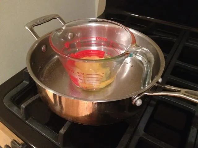 Double boiler setup with a glass measuring cup inside a metal pan on the stove.