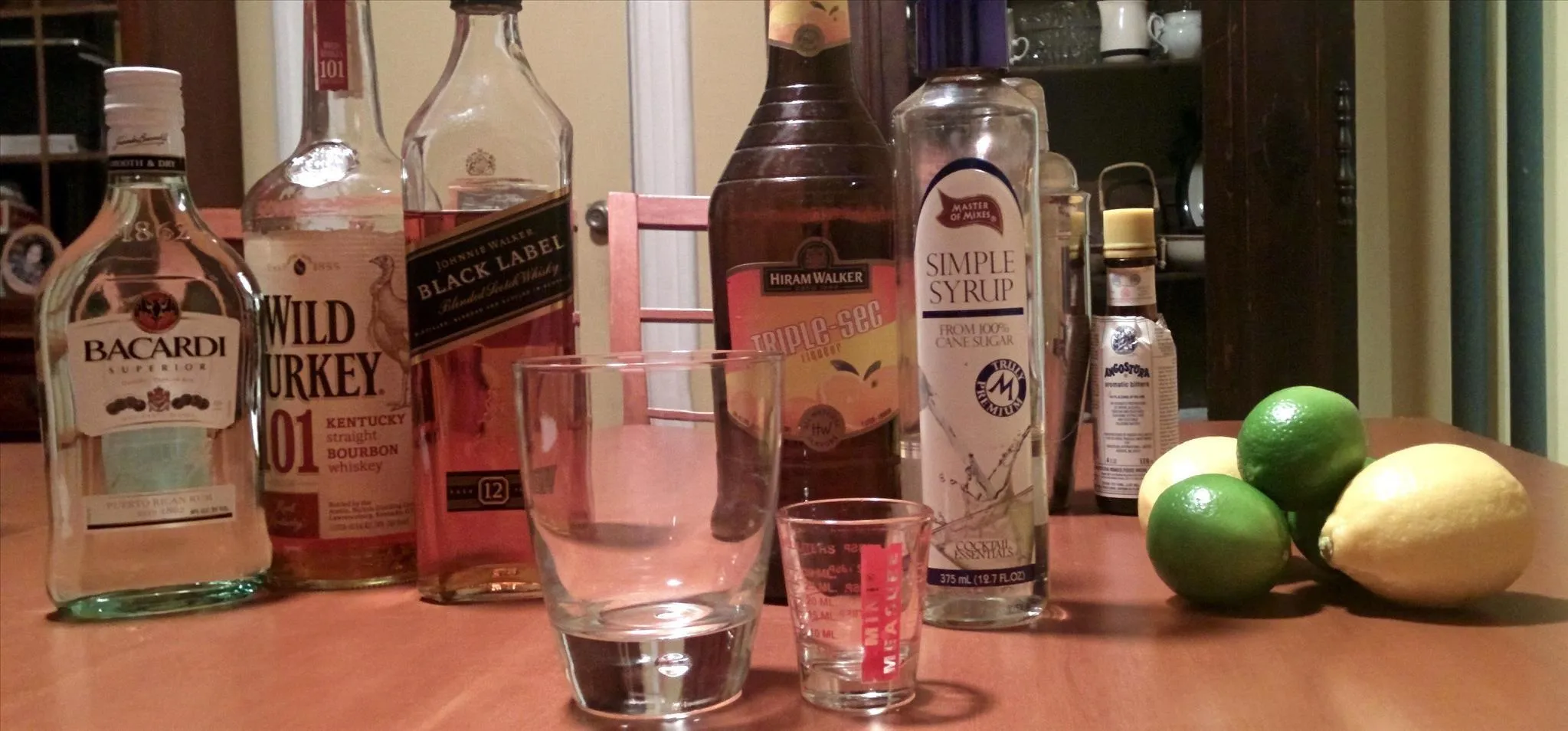 Bottles of various spirits and cocktail ingredients on a wooden table.