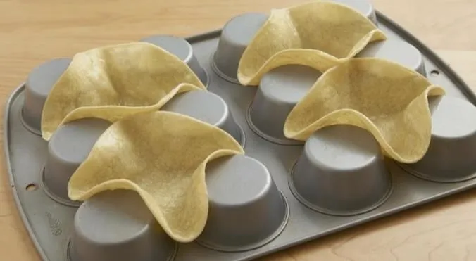 Taco-shaped molds placed in a muffin tin.