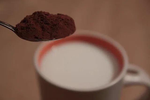 Spoonful of cocoa powder above a cup of milk.