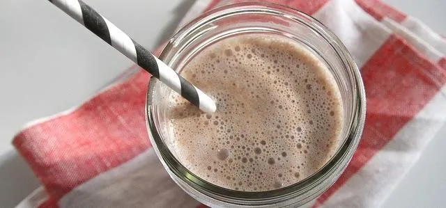 Chocolate smoothie in a glass with a striped straw on a red and white napkin.