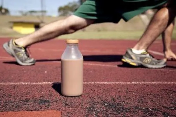 Bottle of protein shake on track with athlete stretching in background.