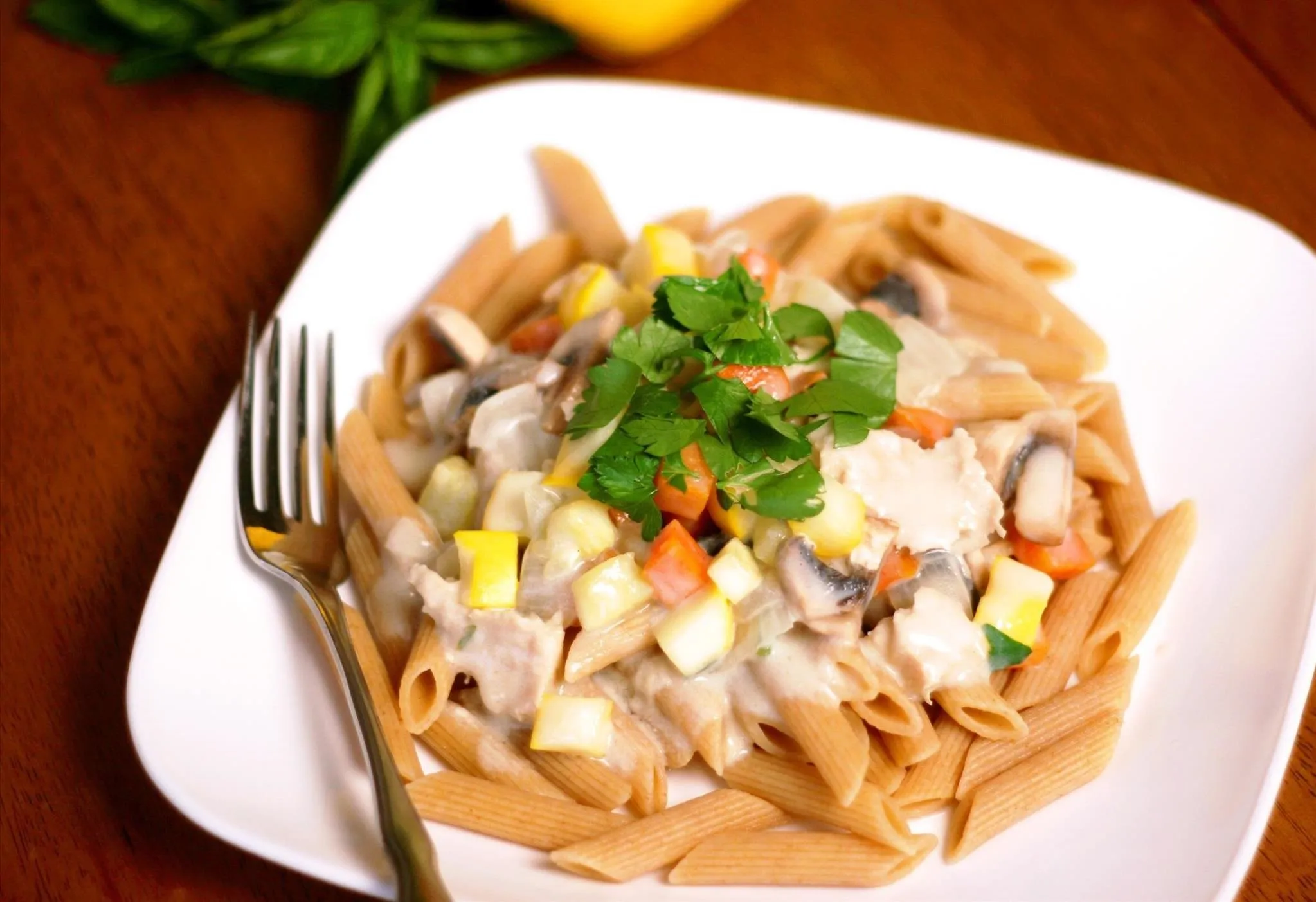 Whole grain pasta with creamy sauce and vegetables, garnished with fresh herbs.
