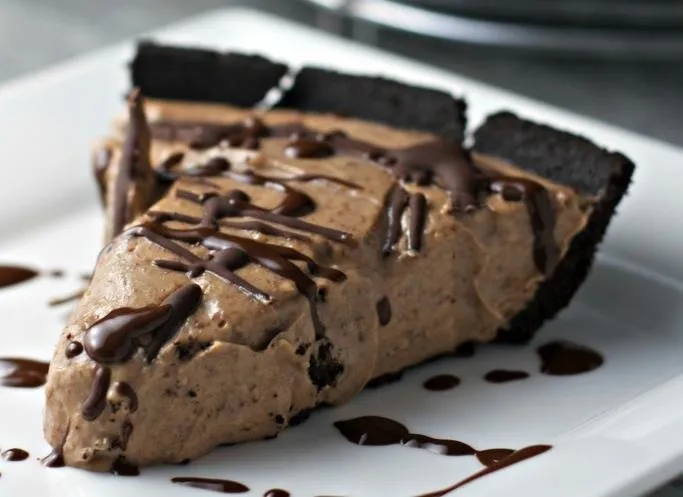 Chocolate mousse pie slice on a white plate with chocolate drizzle.