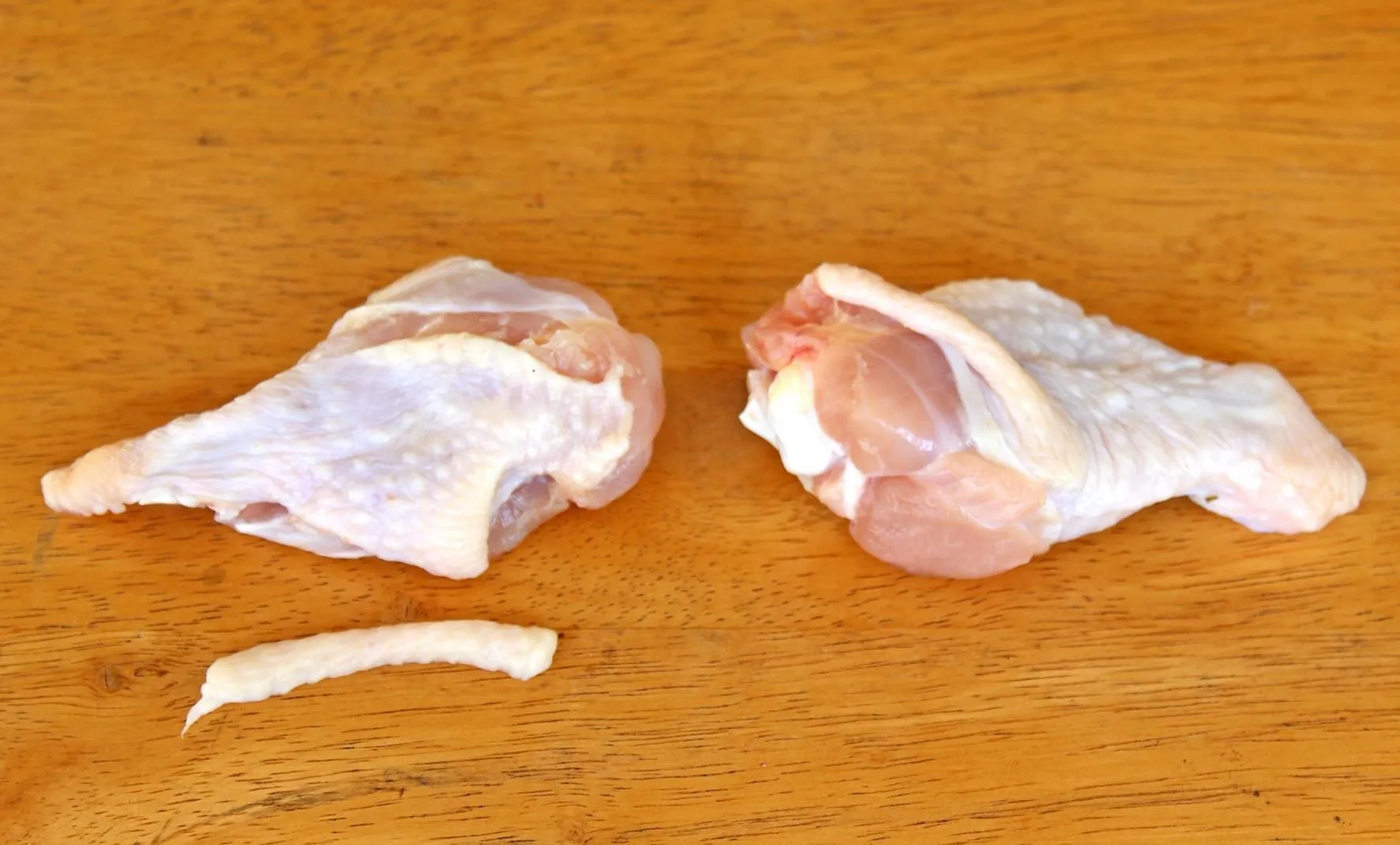 Raw chicken pieces on a wooden surface.