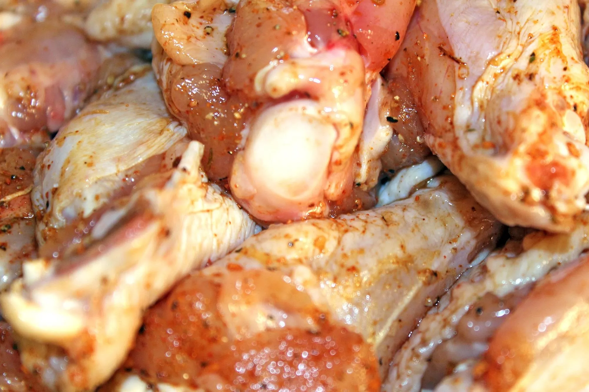 Raw seasoned chicken drumsticks stacked close together.