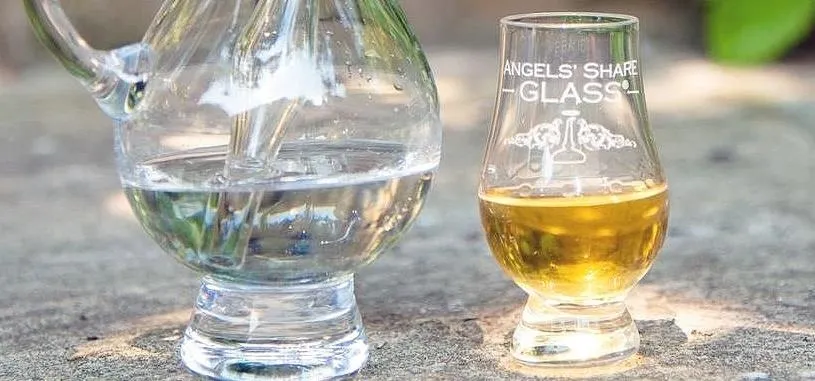 Glass pitcher with water and a small glass of whiskey on a stone surface.