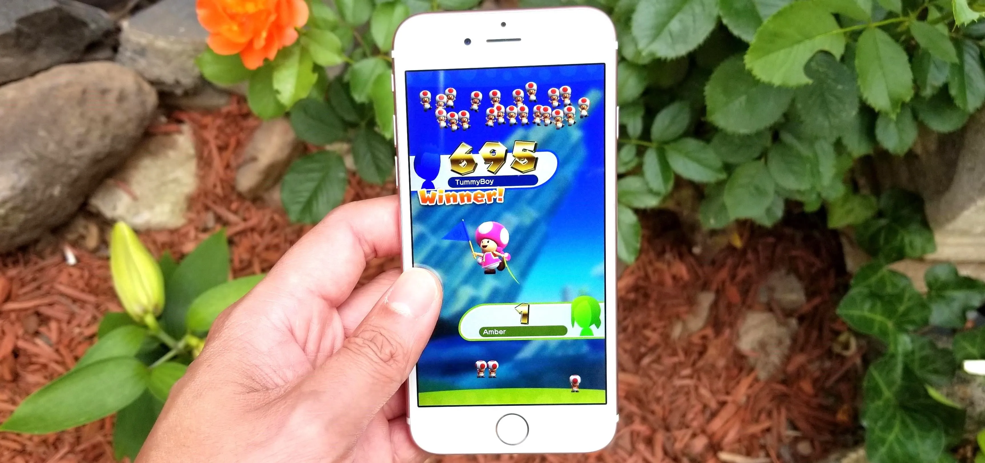 Person holding a smartphone displaying a colorful mobile game in a garden setting.