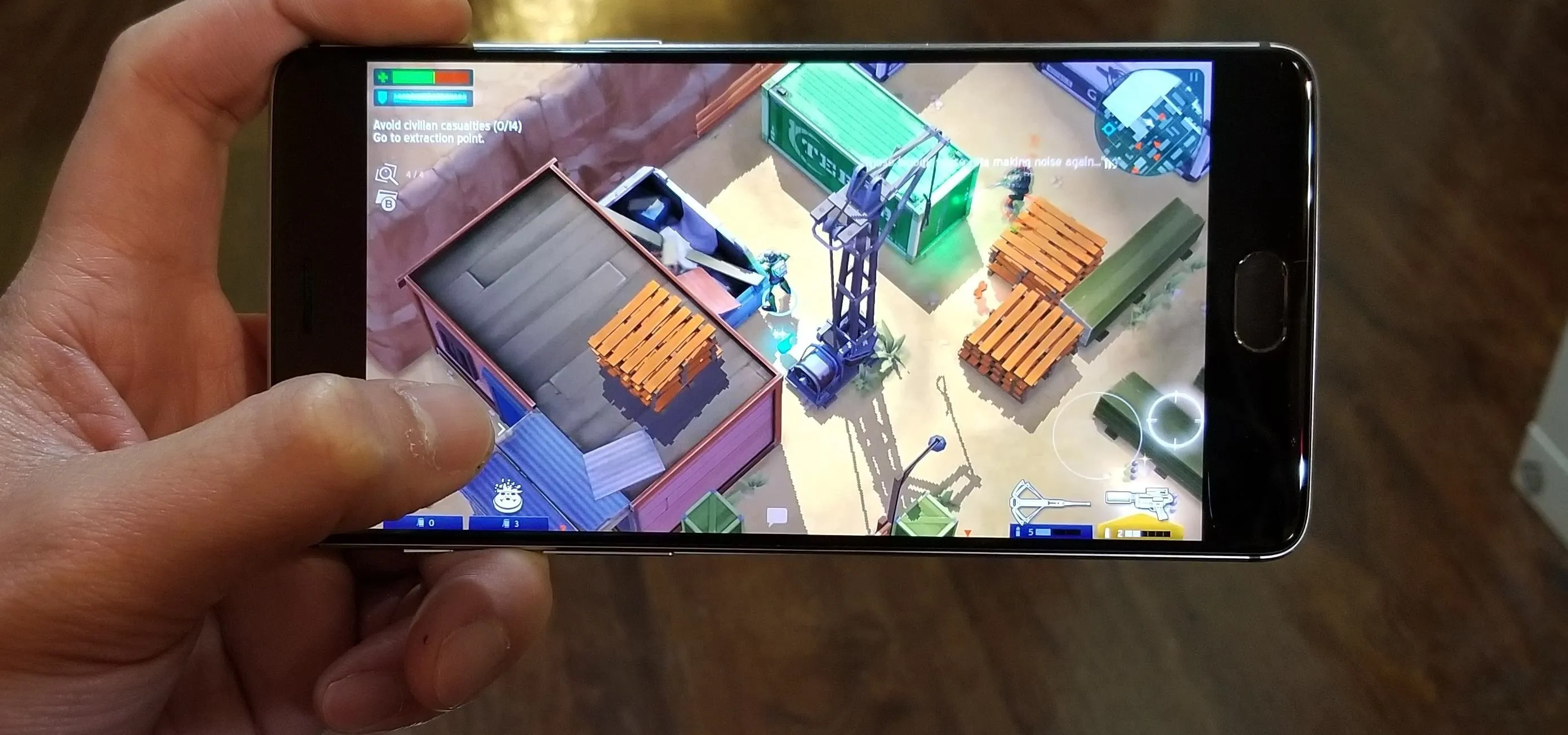 A person playing a mobile video game featuring a top-down view of a construction site with crates and machinery.