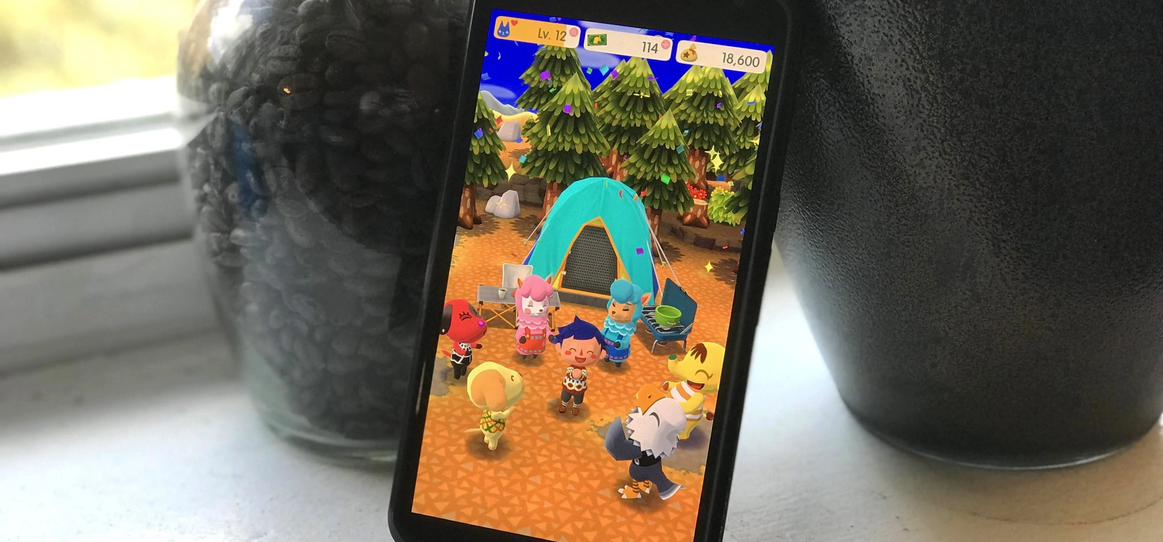 A smartphone displaying a colorful animated scene with characters near a tent in a garden setting.