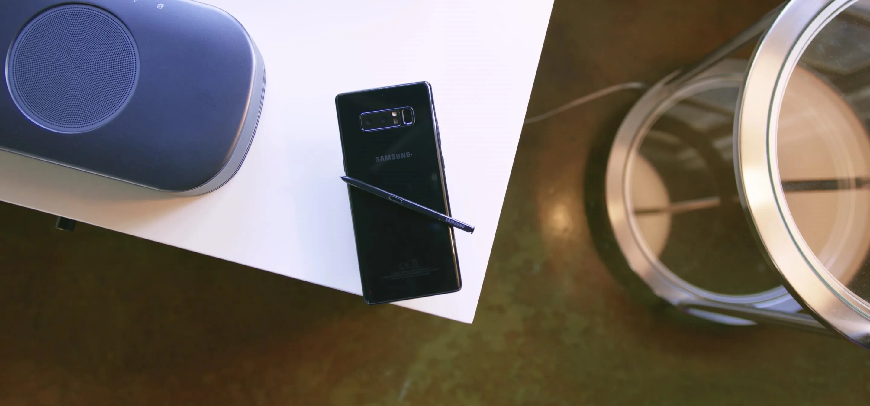Smartphone with stylus on a table next to a speaker and a cup.