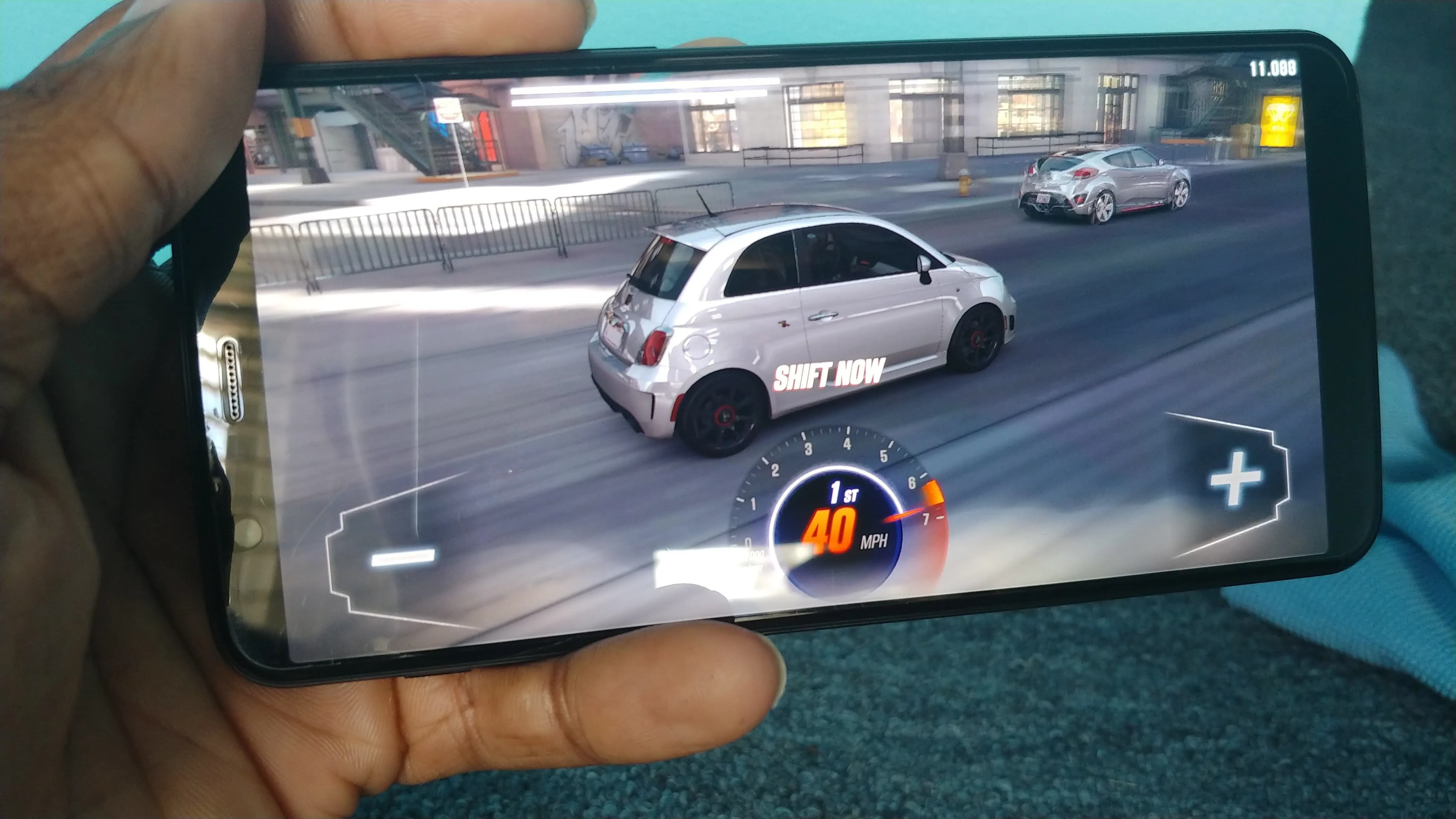 A person holding a smartphone displaying a racing game with a car on a track.