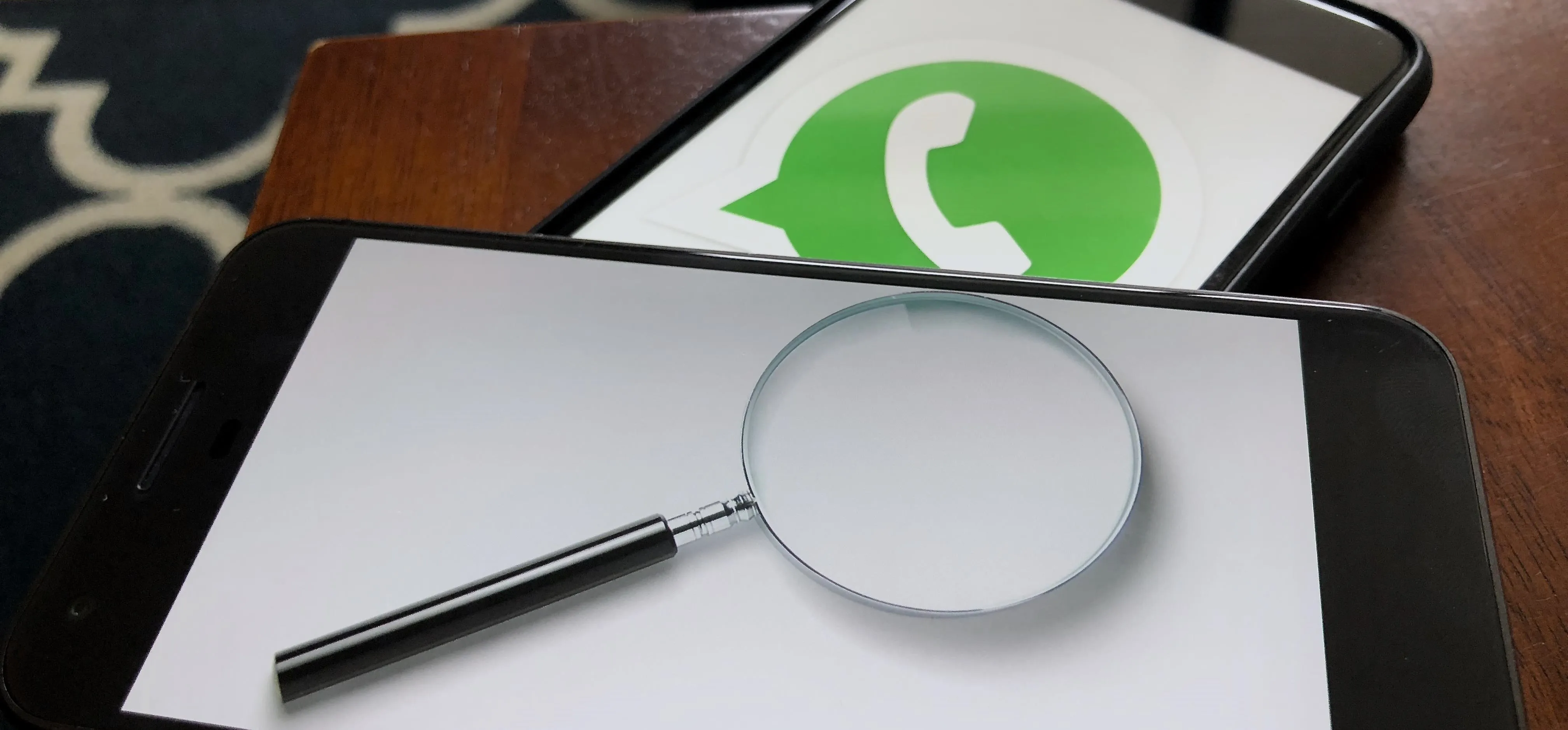 Magnifying glass on a smartphone displaying the WhatsApp logo.
