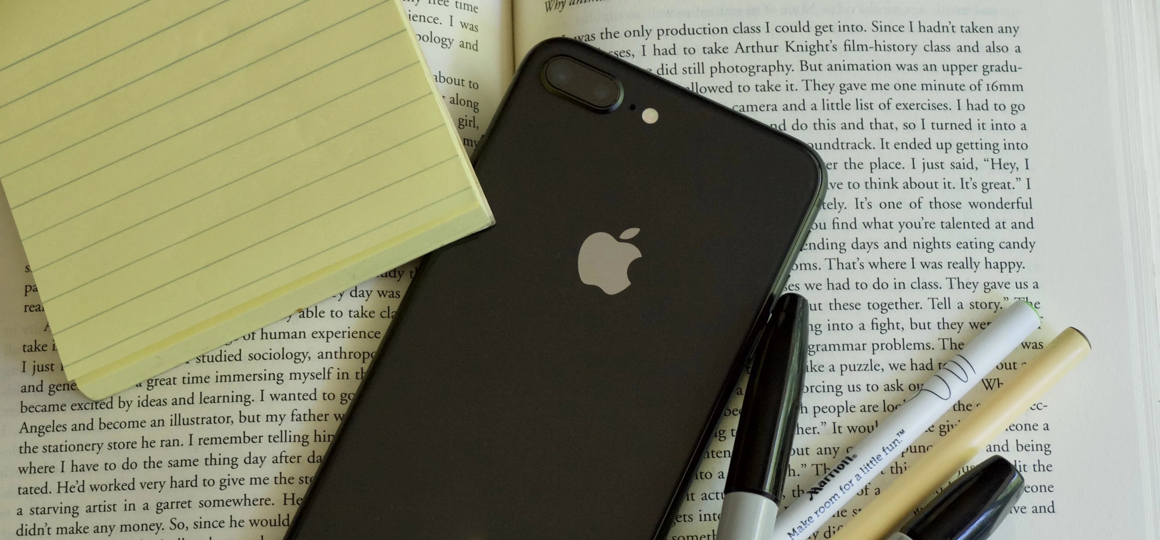 Smartphone on a book next to notepad and pens.