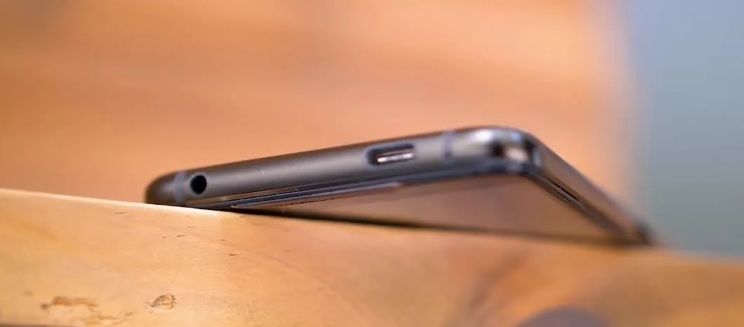 Smartphone lying on a wooden surface, showing its side profile and audio jack.