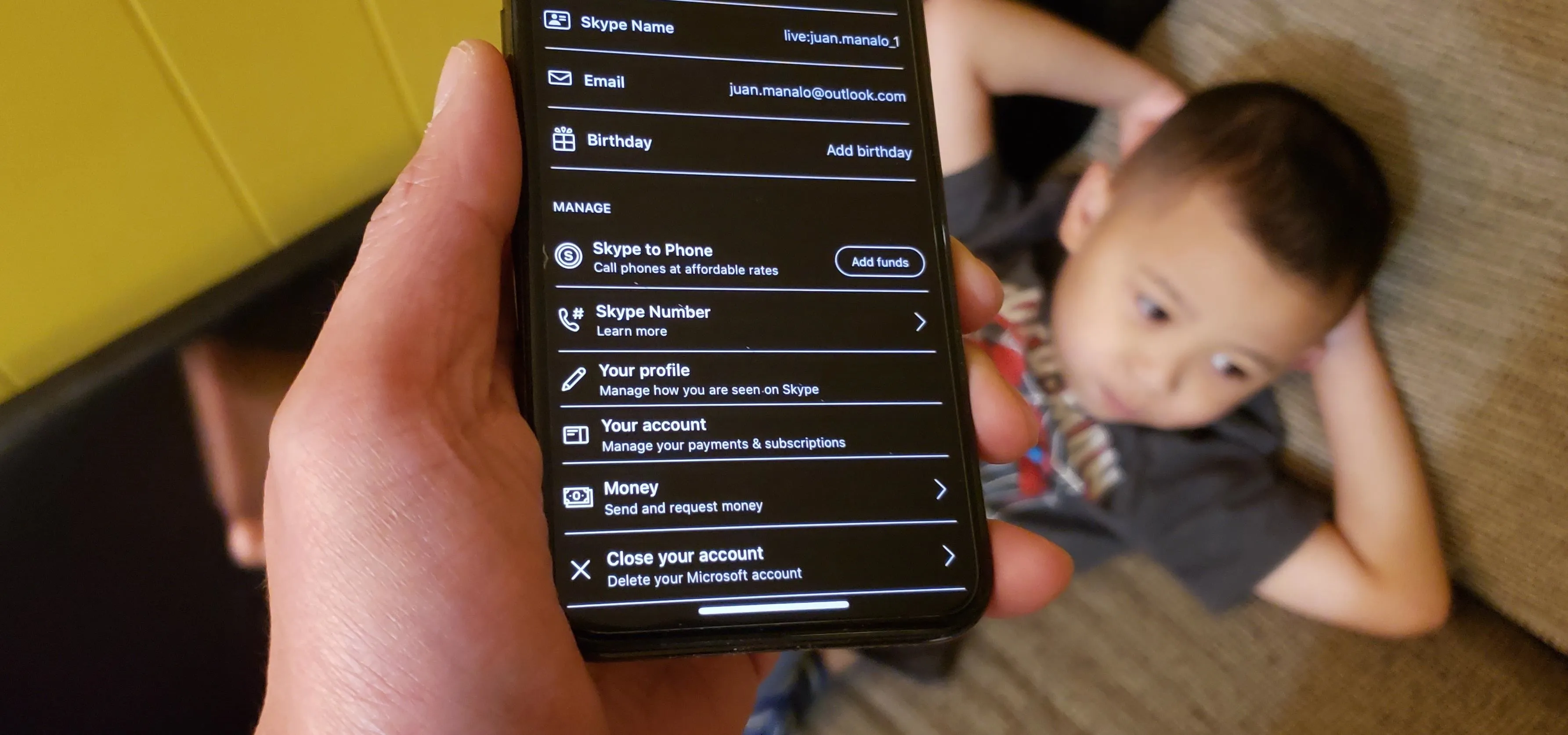 Child relaxing with a phone displaying settings menu.