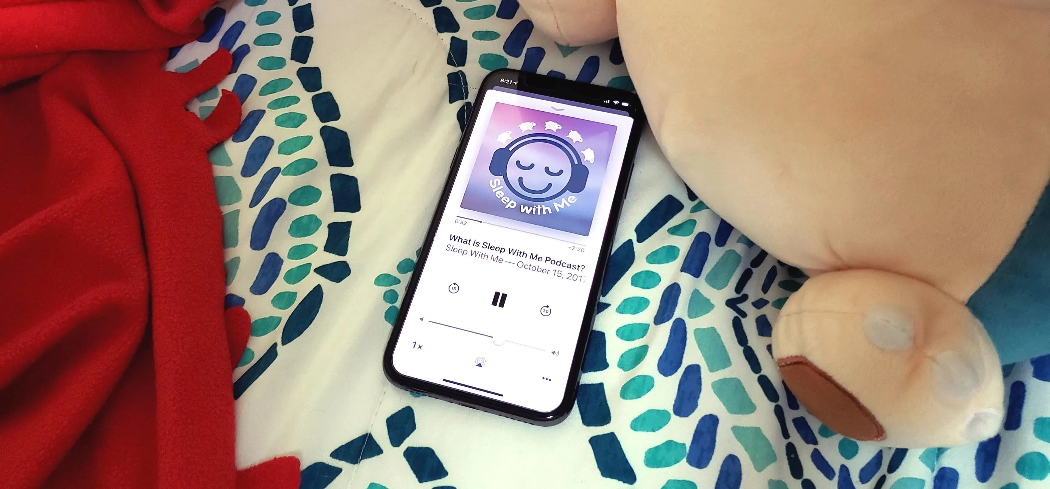 A smartphone displaying a music app, resting on a colorful patterned bedspread next to a stuffed animal.