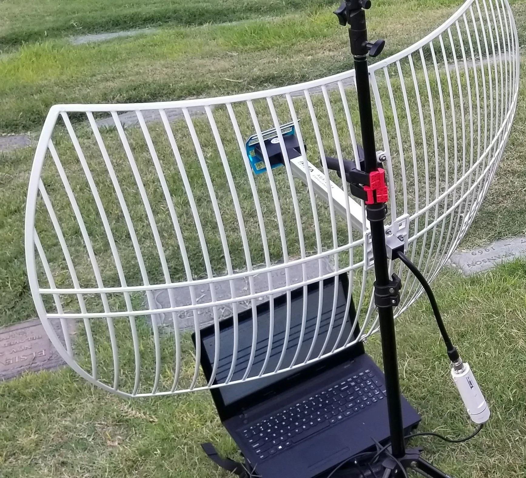 Antenna setup on a stand with a laptop below on grass.