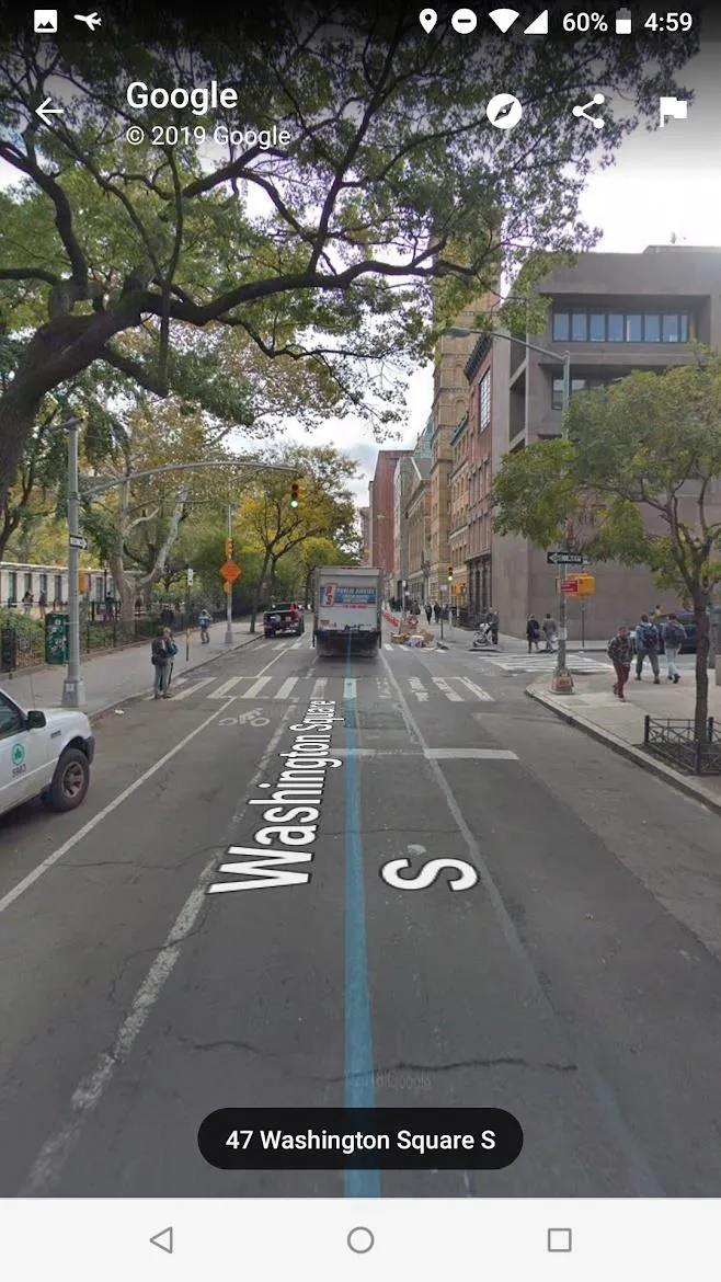 City street view with trees, sidewalks, and parked vehicles.