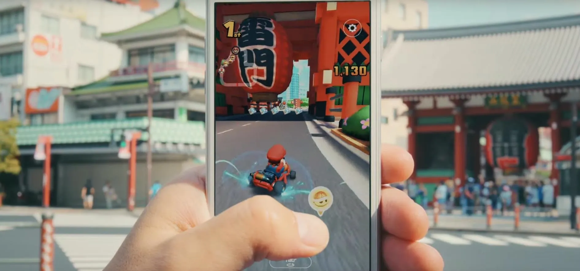 Person holding a smartphone displaying a racing game with a street scene in the background.