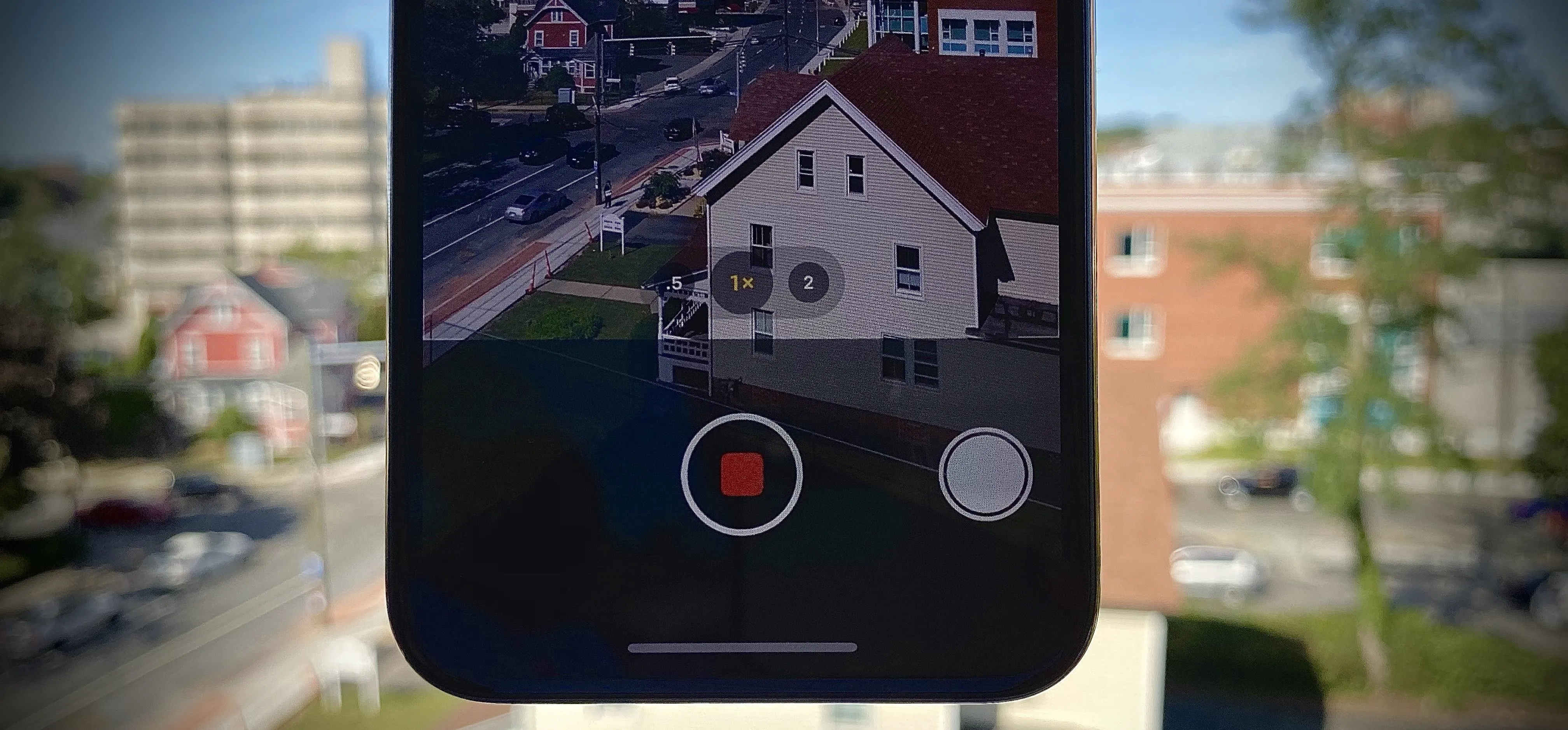Smartphone camera interface showing a recording in progress with a view of buildings and a house.