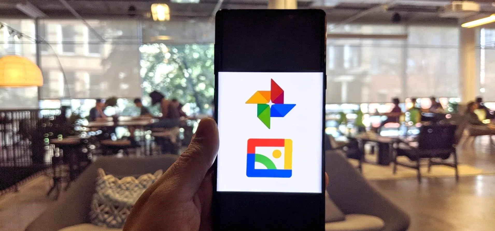 A person holding a smartphone displaying the Google Photos logo in a modern workspace.