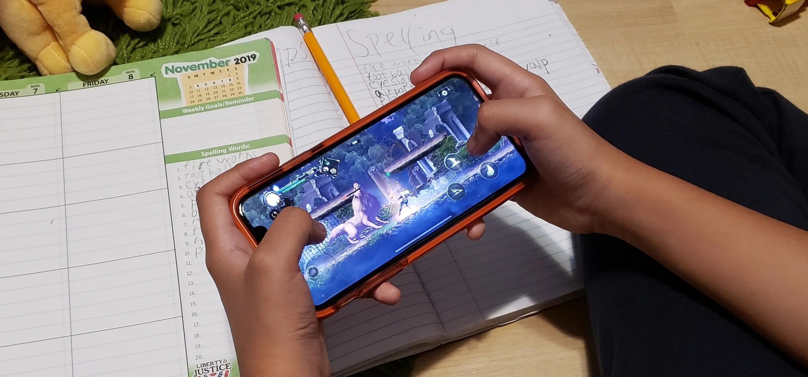 Person playing a mobile game while studying with an open notebook and pencil nearby.