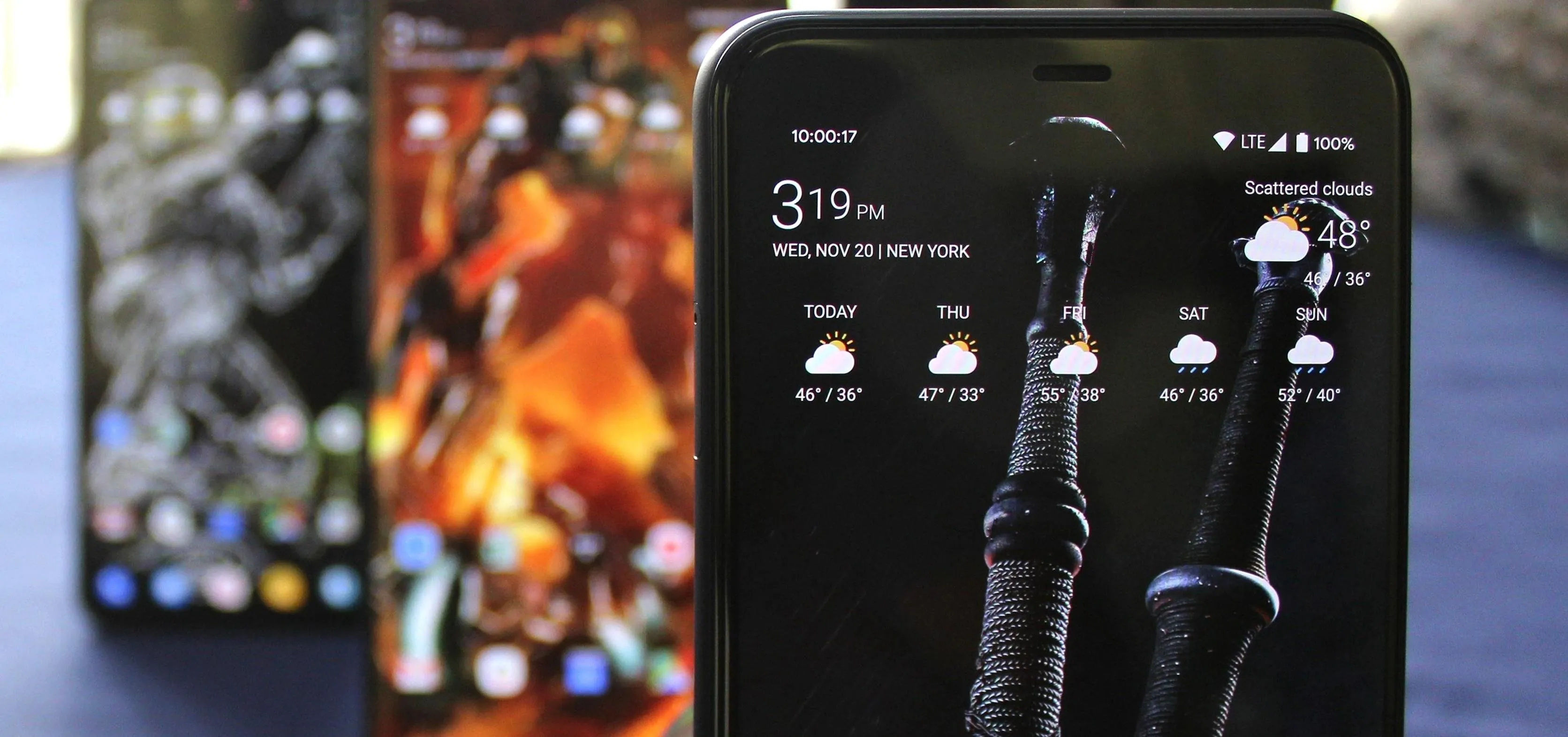 A close-up of a smartphone displaying a weather app, with two other smartphones in the background.