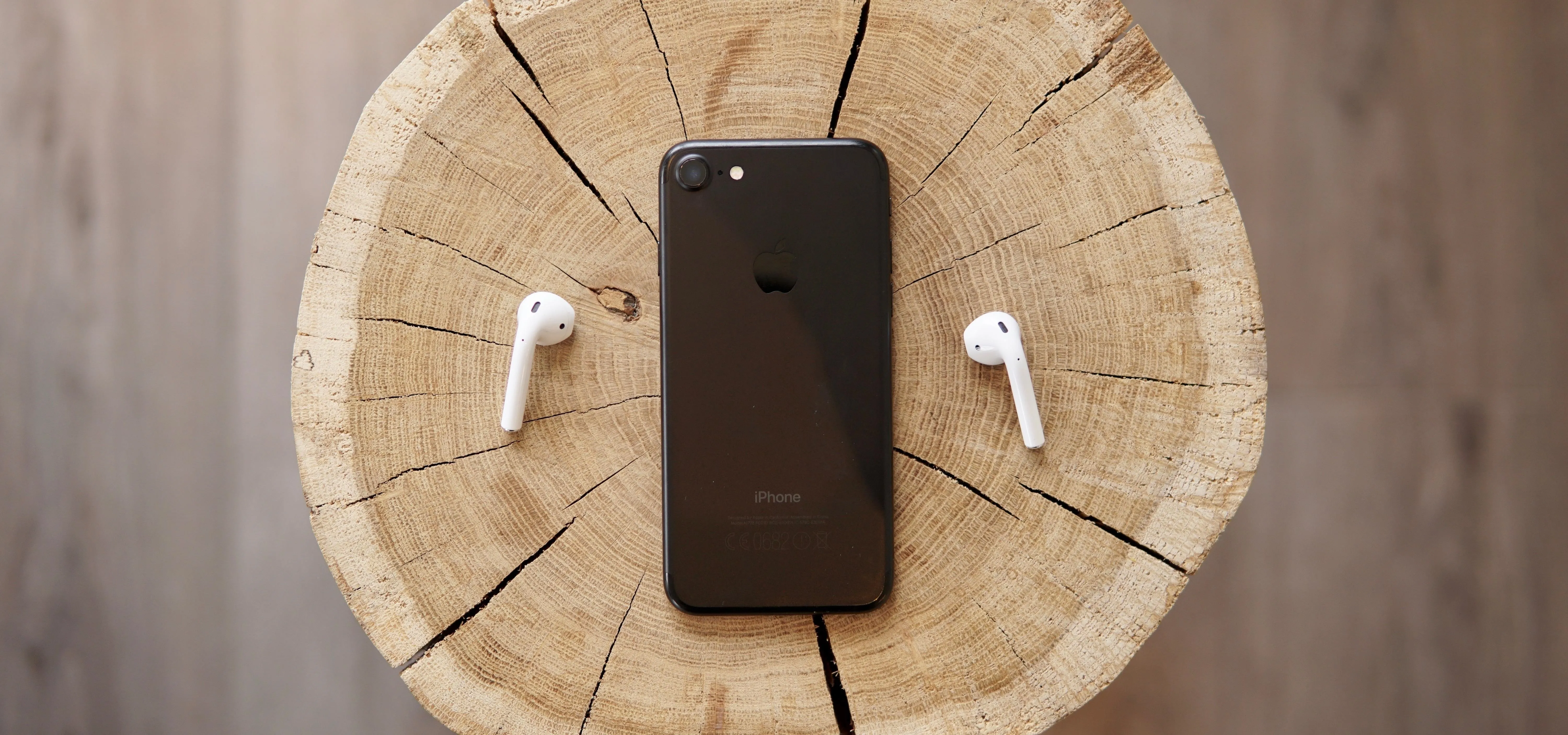 Smartphone and wireless earbuds on a wooden surface.