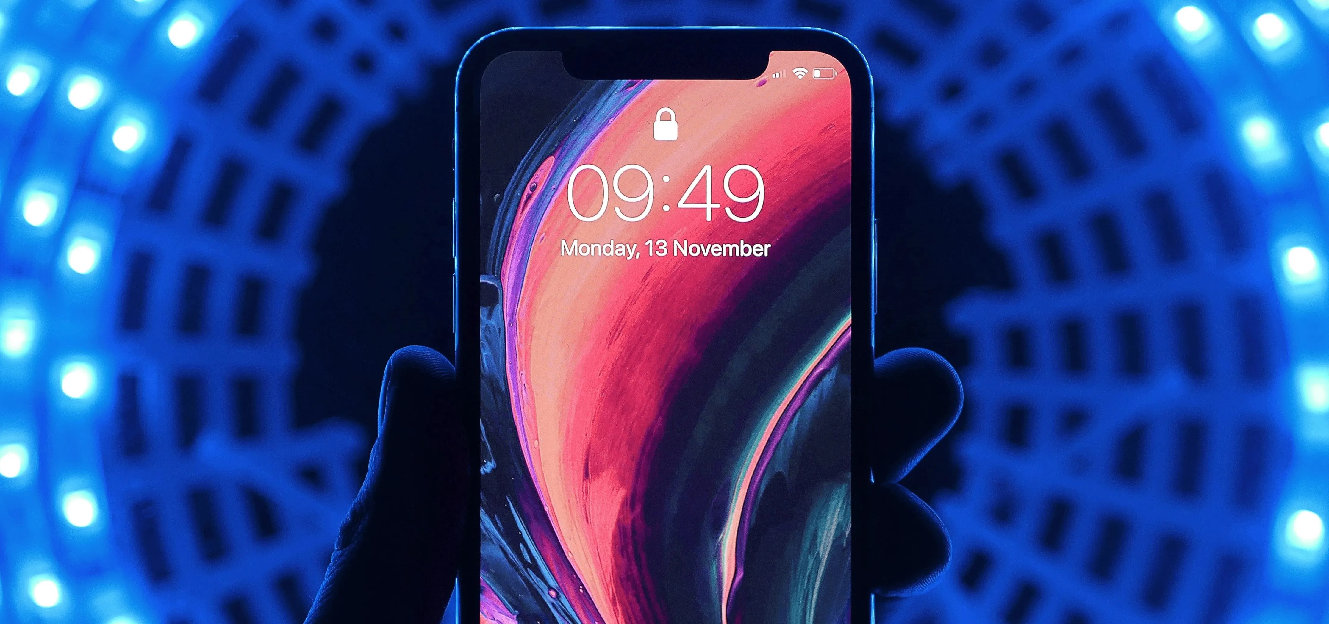 Smartphone displaying the time and colorful abstract wallpaper against a blue illuminated background.