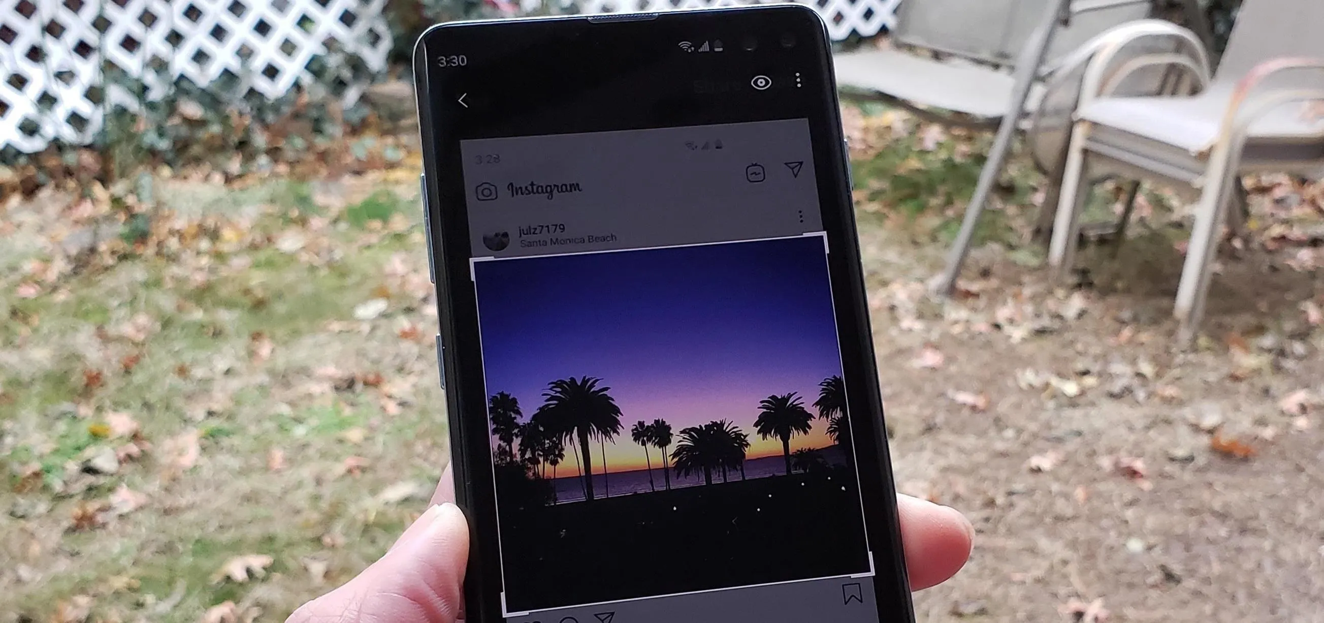A hand holding a smartphone displaying a sunset with palm trees.