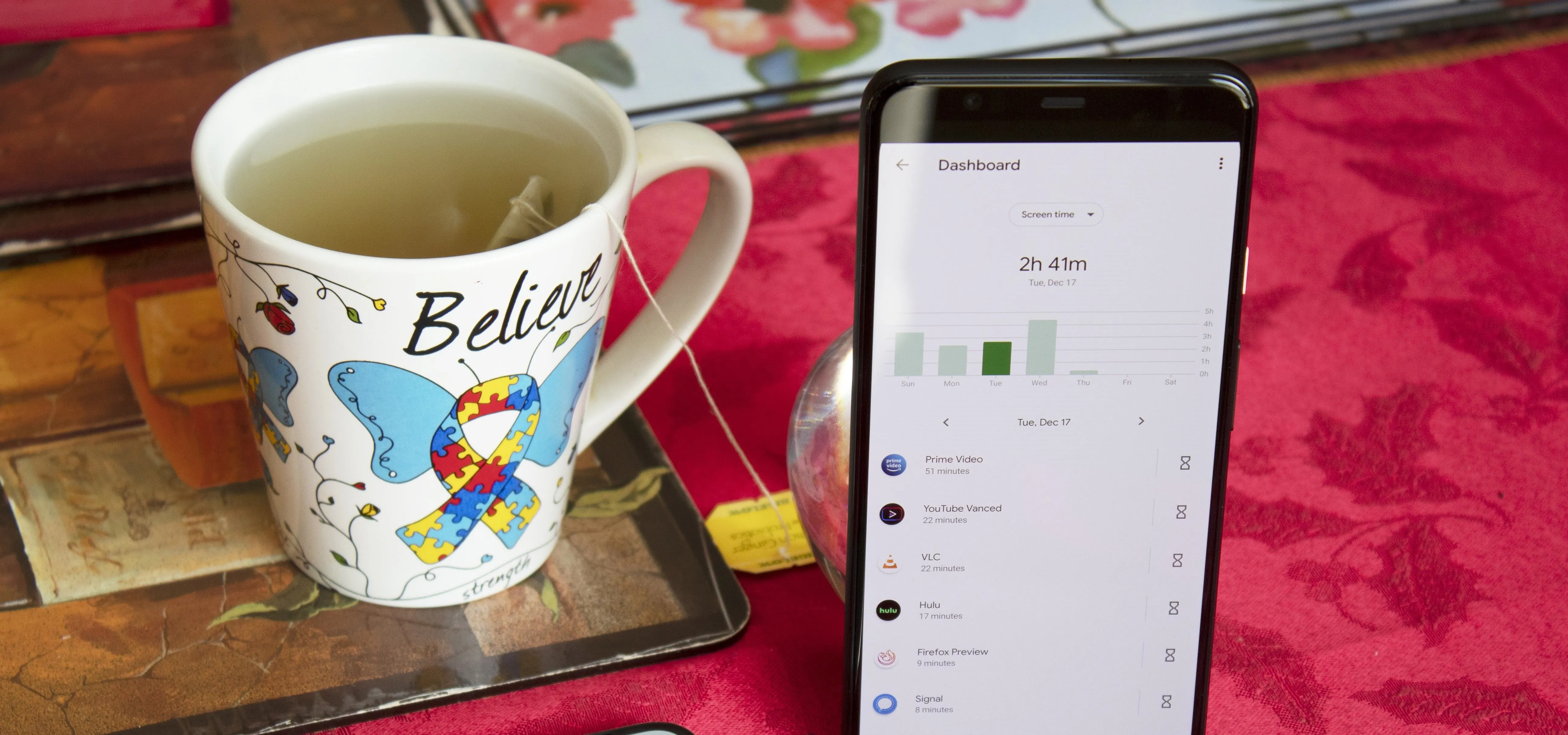 Cup of tea next to a smartphone displaying an app on a table with a floral background.