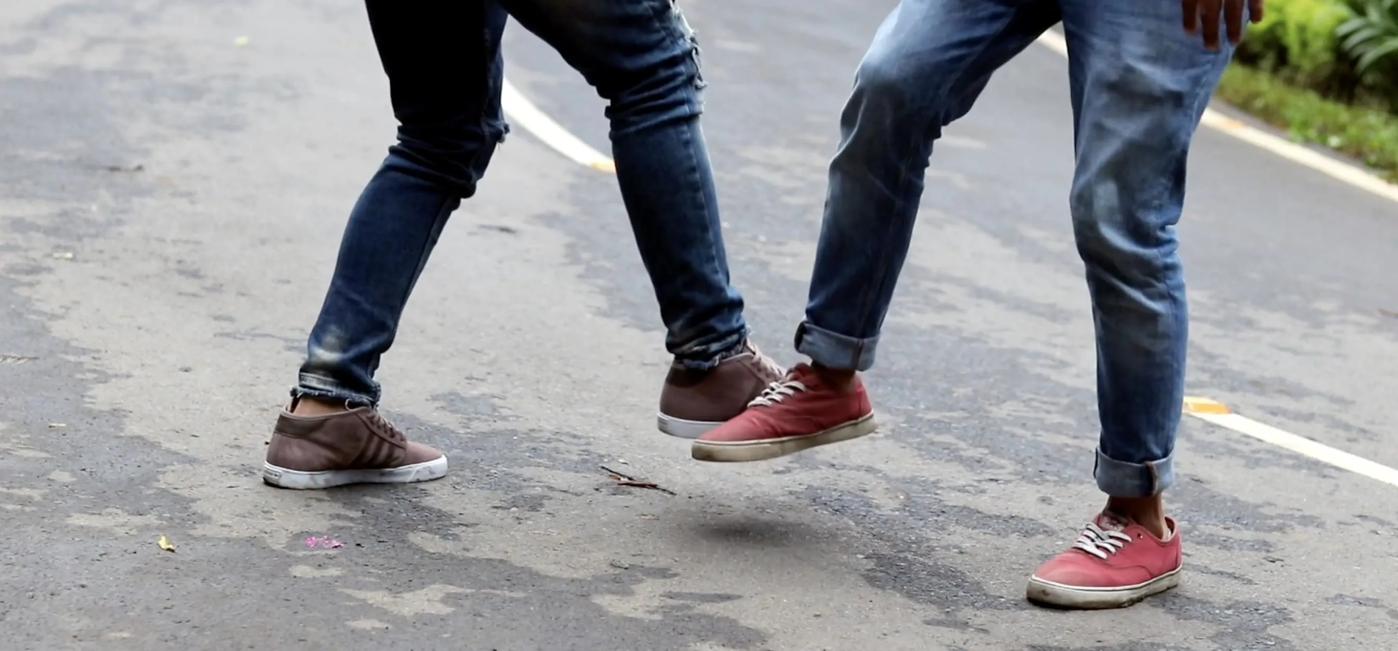 Two pairs of feet wearing casual shoes, playfully tapping on a road surface.