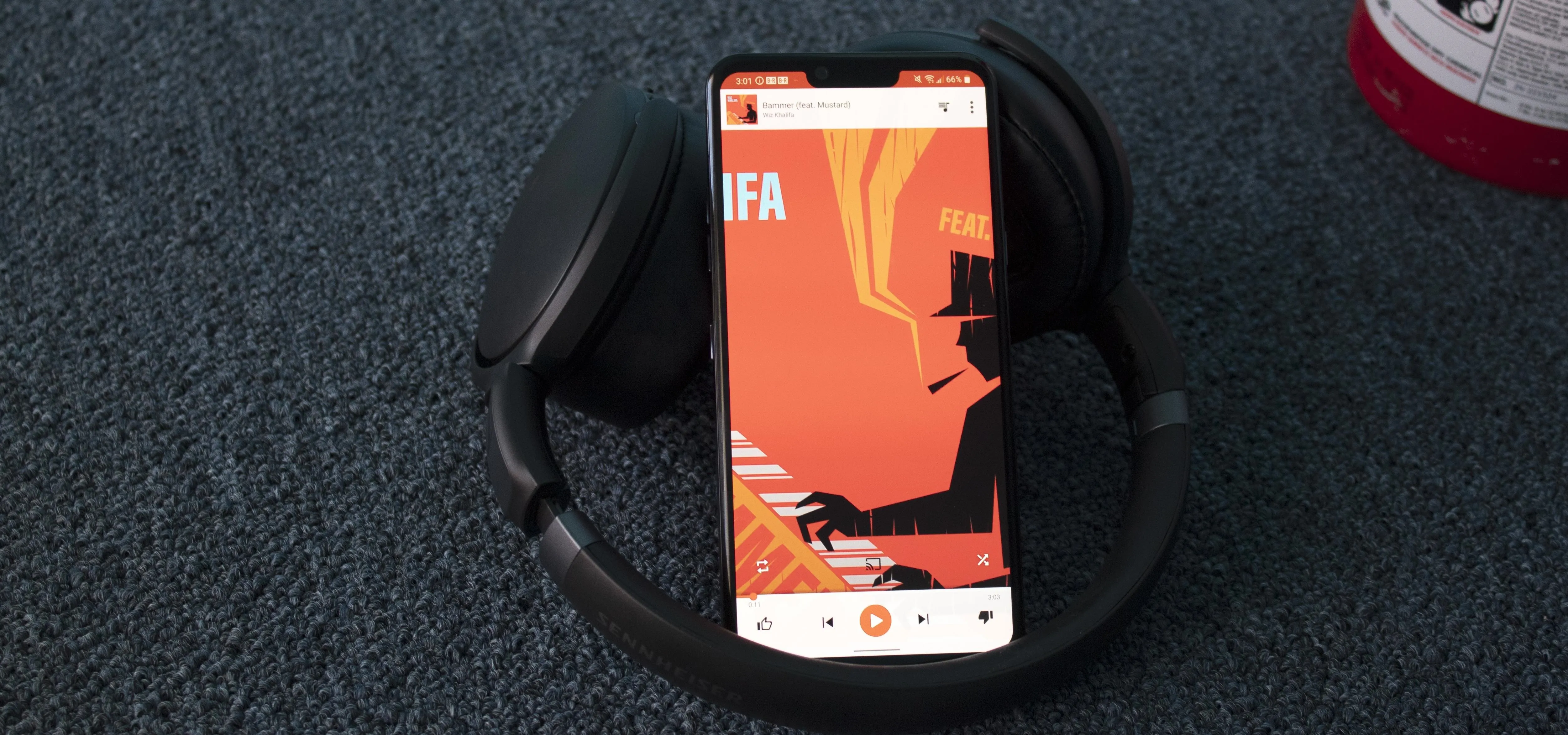 Mobile phone displaying music app on a soft surface next to headphones.