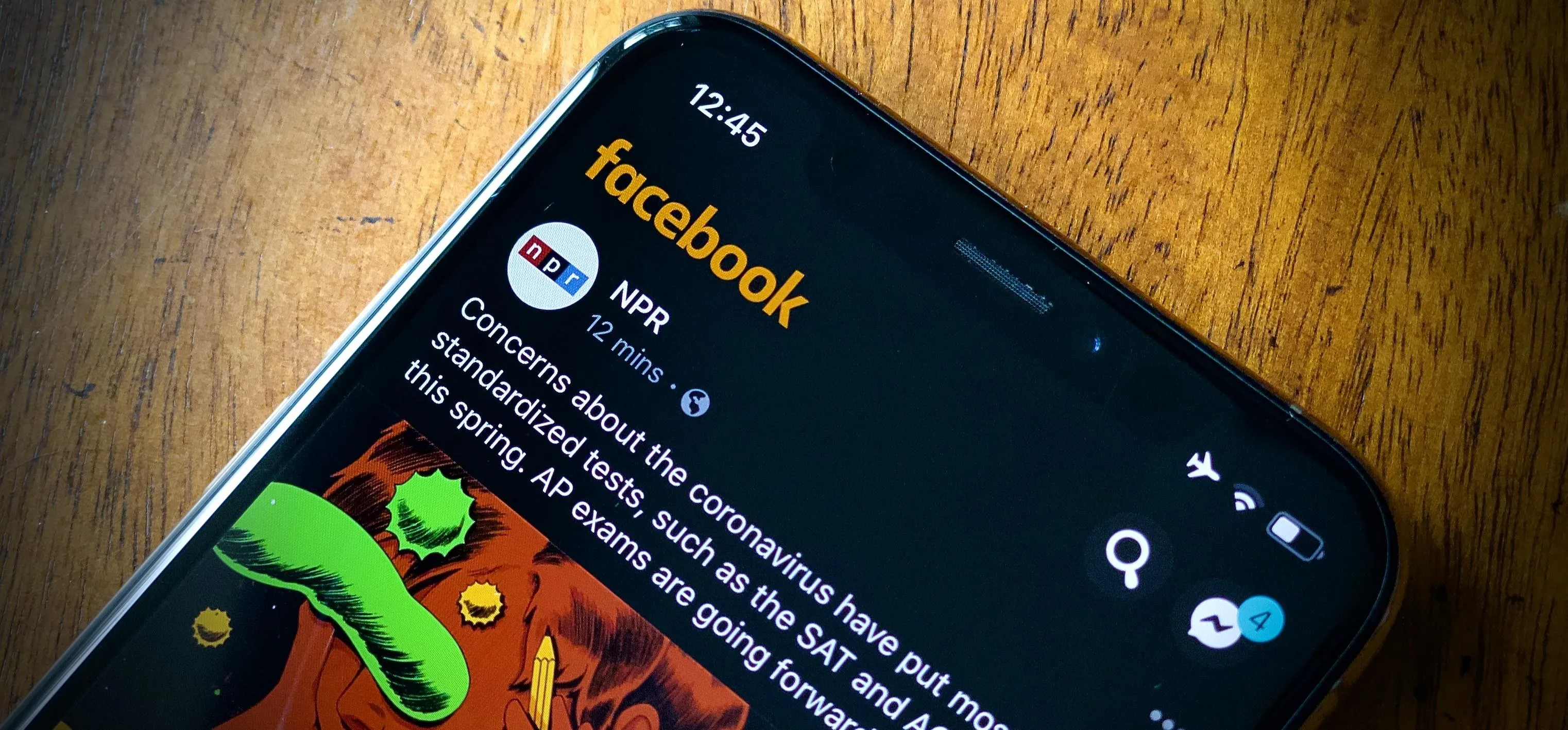 Close-up of a smartphone displaying a Facebook post on a wooden surface.
