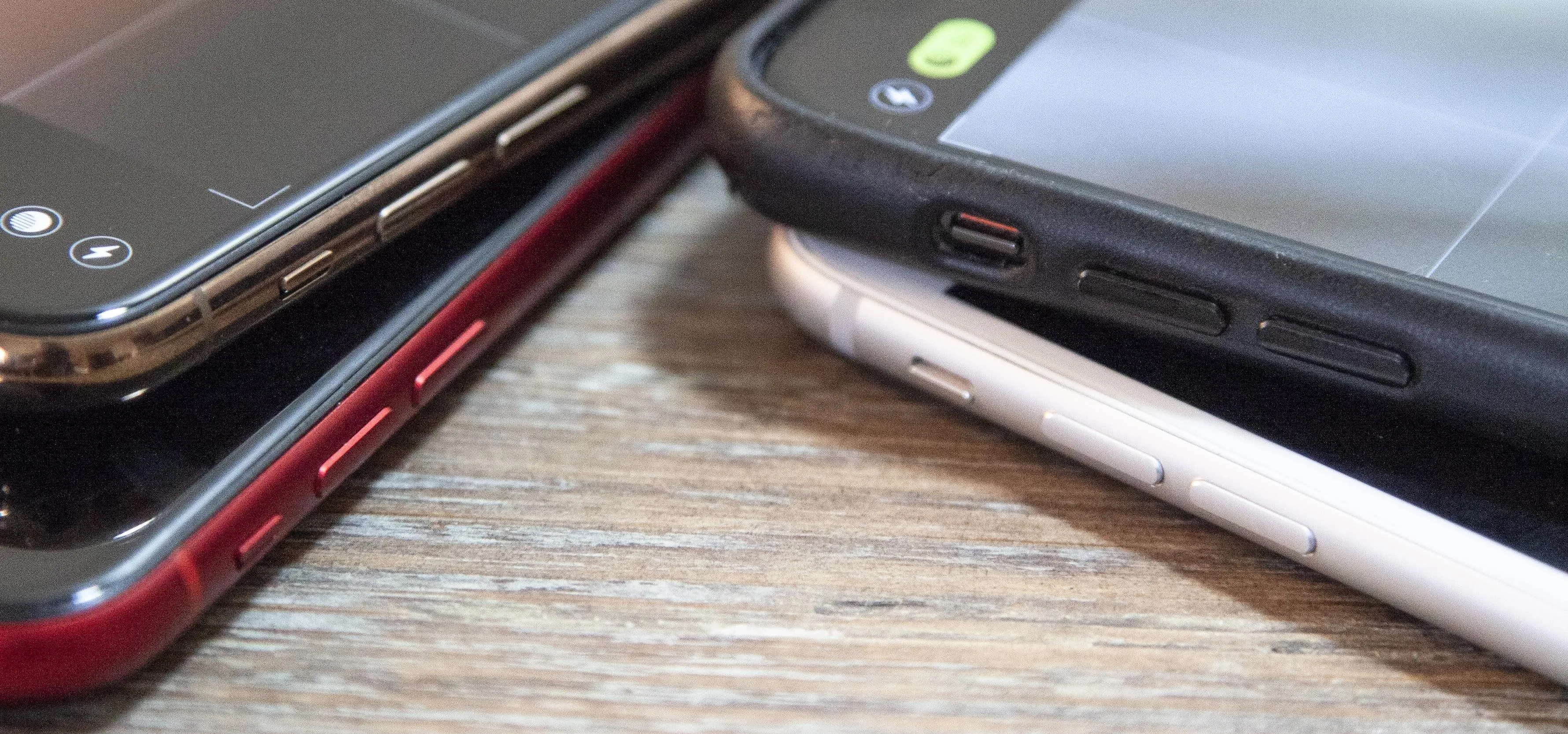 Smartphones stacked on a wooden surface.
